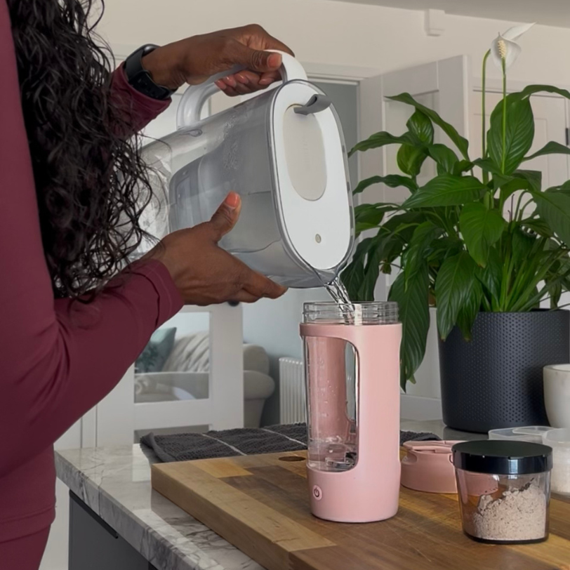 person pouring water from water purifier jug into USB electric protein shaker with protein powder box on the side